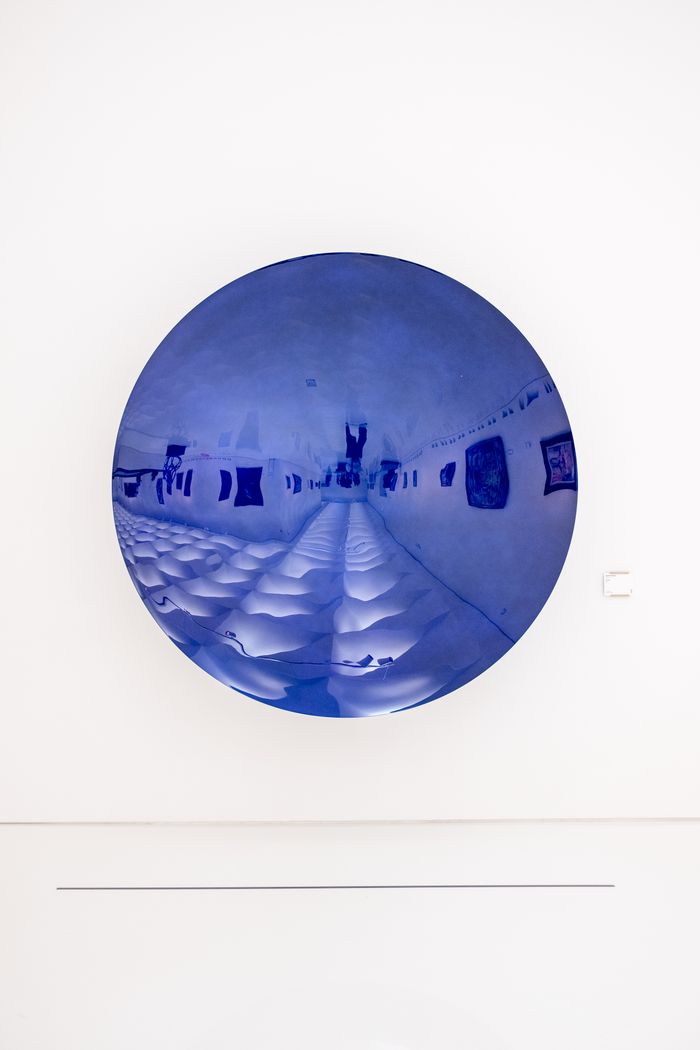 Abstract blue circular art piece on white wall in contemporary museum setting.